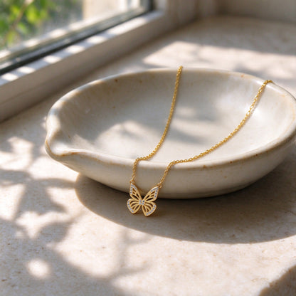 Aurelia gold butterfly necklace draped over a ceramic jewellery dish