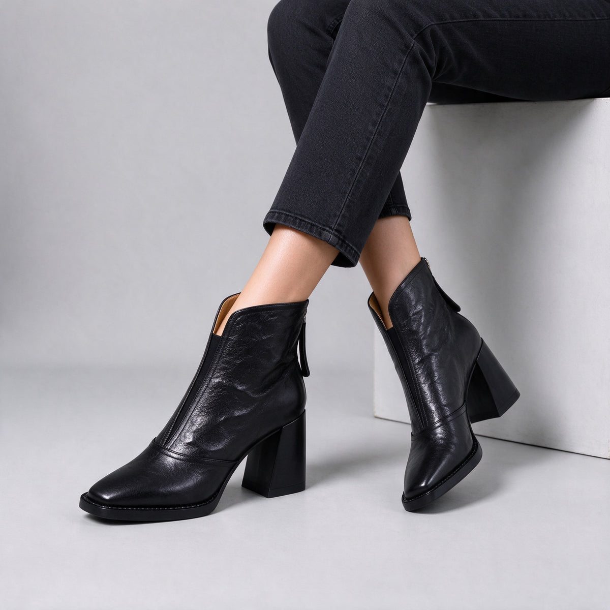 Livia black leather ankle boots worn seated with crossed ankles